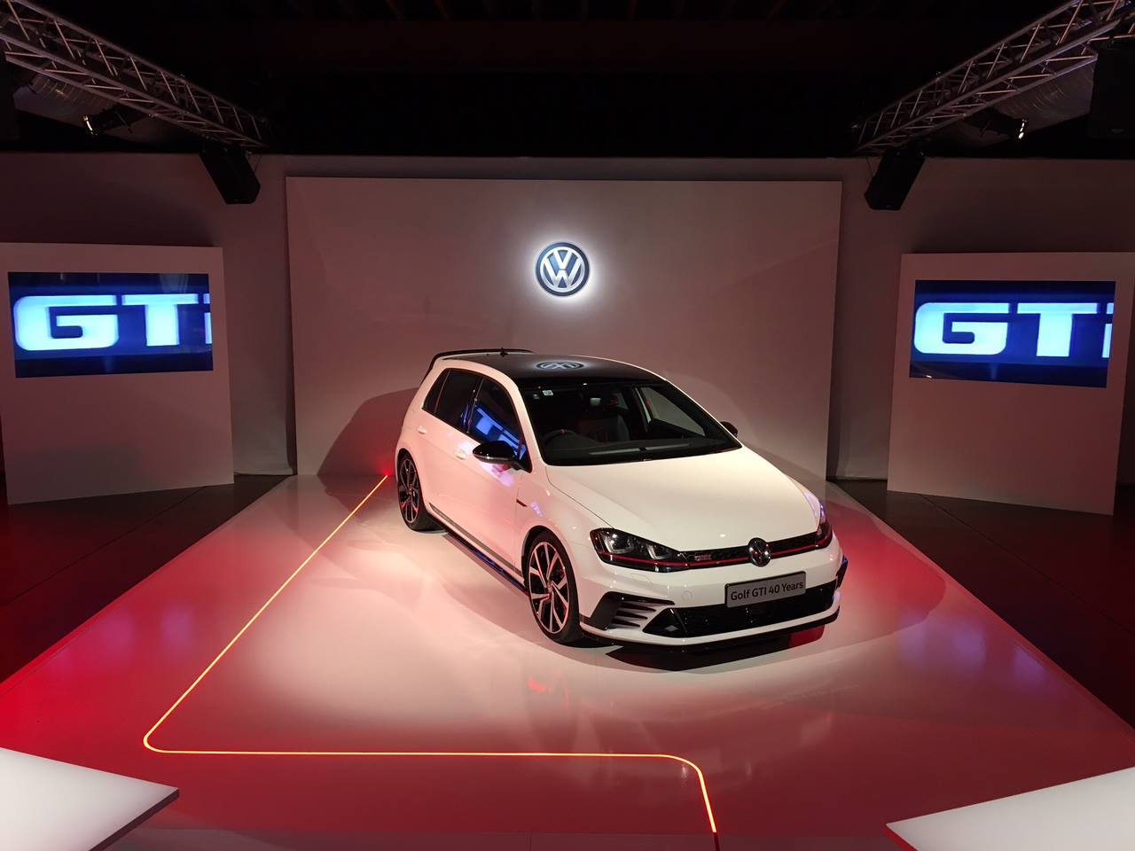 White VW Golf GTI on a lit stage with GTI screens either side